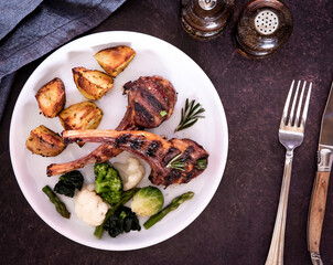 Top down view of a plated grilled lamb chops meal with potatoes and vegetables.