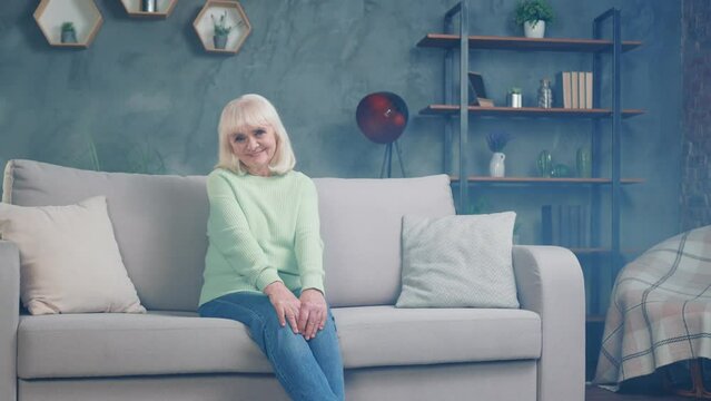 Gorgeous grey haired granny in good mood sitting cozy divan spacious loft