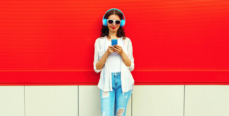 Portrait of smiling young woman in headphones listening to music with phone on red background