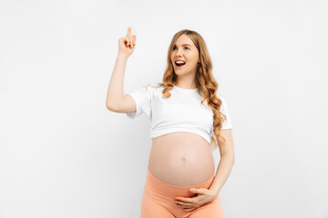 happy pregnant woman standing against. .Cheerful young woman with open mouth pointing up and having...
