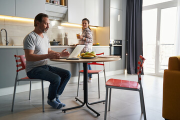 Man working with laptop while his wife cooking