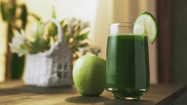 Delicious green smoothie with cucumber and apple in the glass, on the background of morning window and flowers. Concept of healthy eating.