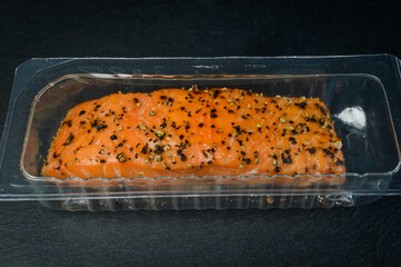 hot smoked salmon steak flavored with black pepper in its protective clear plastic packaging on a slate tray