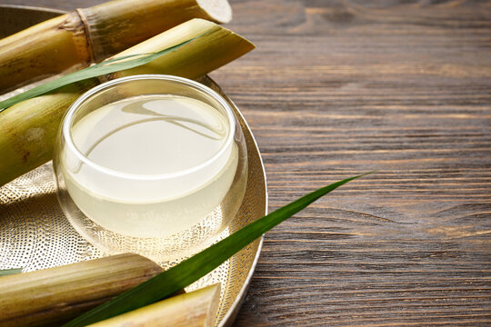 Sugarcane and fresh cane juice in a metal tray on a wooden background with space for text.