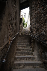 Stone steps rise up in a narrow dark passage between the walls of old houses