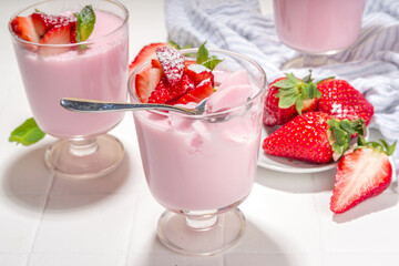 Homemade sweet strawberry panna cotta dessert, pink Italian panna cotta in three glasses, with fresh sliced strawberry and mint on white tiled background copy space