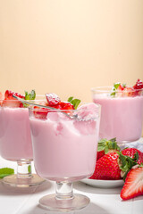 Homemade sweet strawberry panna cotta dessert, pink Italian panna cotta in three glasses, with fresh sliced strawberry and mint on white tiled background copy space