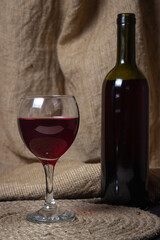 A glass of red wine on a background of burlap. Bottle of red wine. Exquisite alcoholic drink.