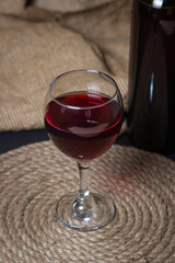 A glass of red wine on a background of burlap. Bottle of red wine. Exquisite alcoholic drink.