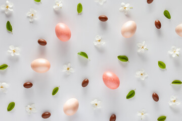 Easter background. Pattern made of eggs, flowers and candies on a white background. Flat lay.