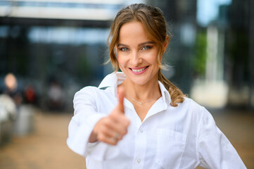 Confident young female manager outdoor in a modern urban setting giving thumbs up