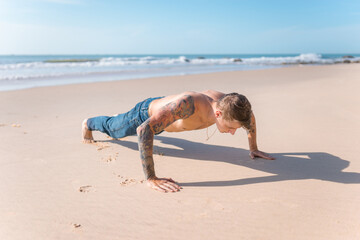 Handsome young caucasian bare-chested man doing push ups on the beach