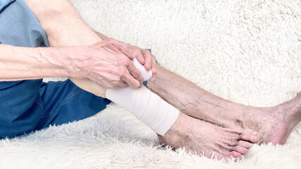 Cropped shot of elderly man sitting on sofa and suffering from leg pain. Leg with bandage. Bone...