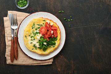 Rustic omelette or frittatas with green onions, cheese mozzarella, green arugula and tomatoes on old wooden dark background. Healthy food concept. Breakfast. Copy space. Top view. Mock up.