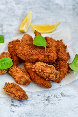 
 Crispy  deep fried   chicken strips and wings . Breaded  with cornflakes chicken  breast fillets  with lemons s and fresh   basil on wooden rustic background