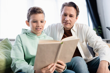 Obraz premium Preteen kid and father reading blurred book in living room