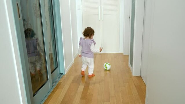 Cute baby girl kicking a soccer ball with leg at apartment corridor - slow motion