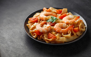 Fettuccine pasta with shrimp and tomatoes on gray plate, on dark background, selective focus, bokeh effect.