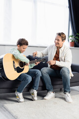 Positive dad pointing at acoustic guitar near son at home