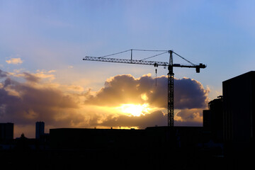 Silhouette industrial crane construction site with sunset and clouds in the background