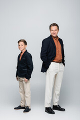 Trendy man posing near preteen son on grey background