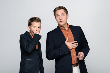 Shocked preteen boy and father looking at camera isolated on grey