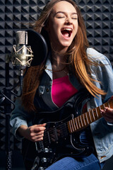 Fototapeta premium Girl musician in recording studio playing electric guitar and singing in mic