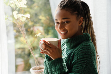 Young black woman with pigtails smiling while drinking tea