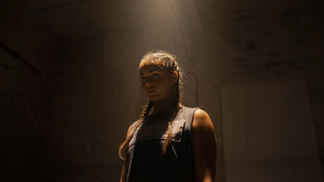 Isolated Confident Looking Female Kick Boxer Standing in the Middle of a Boxing Ring, Looking Directly at the Camera, Confident and Badass. Light Shining On Her From the Top With Fog Surrounding.