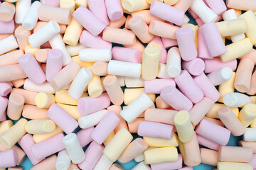 multi-colored marshmallows are scattered over a blue background. Delicious sweet dessert or confectionery addition to cocoa or hot chocolate. Chewing sweets for children. Background of marshmallows