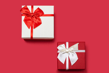 Two white and red gift boxes with ribbons and bows on a red background. Gifts for birthday or traditional holidays. Two gift boxes arranged diagonally with free space for text