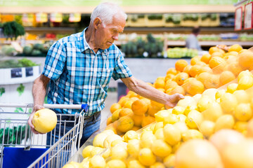 old age man choosing oranges and grapefruits in supermarket