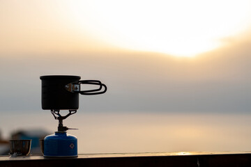 Making coffee outdoors on gas camping fire during beautiful sunrise