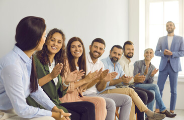Business people clapping in the conference room. Smiling men and women sitting in a row applauding their female colleague at a team meeting. Concept of conferences, seminars, teamwork brainstorming