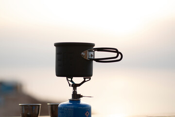 Making coffee outdoors on gas camping fire during beautiful sunrise