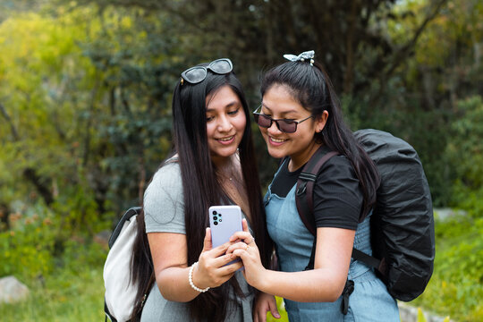 03	Retrato de dos hermosas chicas mirando el móvil en el hermoso parque,
Amigas felices revisando teléfono inteligente en aire libre,Dos chicas usando el móvil en medio de un camino rodeado de montaña