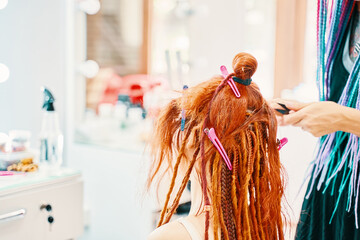 Barber braids dreadlocks. The hairdresser weaves braids with red kanekalon beautiful red-head girl. Beautiful cool hairstyles. Hair service in a beauty salon. Fashionable women's style.