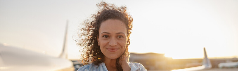 Portrait of relaxed woman smiling at camera while standing outdoors ready for boarding the plane at...