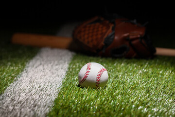 Low angle view of baseball on grass field with stripe and defocused mitt and bat