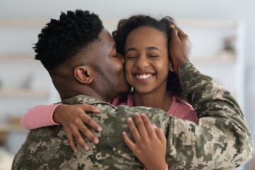 Loving black father in camouflage kissing his daughter