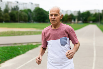 Senior man running on jogging track in nature. Healthy retirement lifestyle