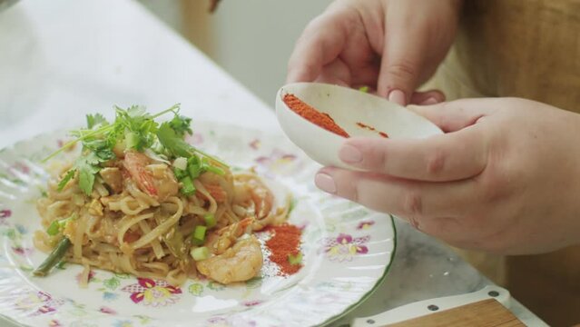 Woman adding ground red pepper to wok noodles