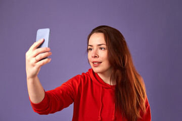 Naklejka premium Close up portrait of caucasian woman in red clothes using her mobile on purple background