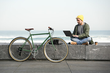 Hispanic freelancer working at the coast beside bicycle. Urban mobility and sustainability concept.
