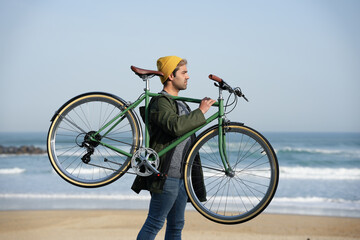 Hispanic man carrying classic bicycle on shoulders at the coast.