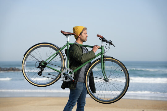 Hispanic man carrying classic bicycle on shoulders at the coast. - Powered by Adobe