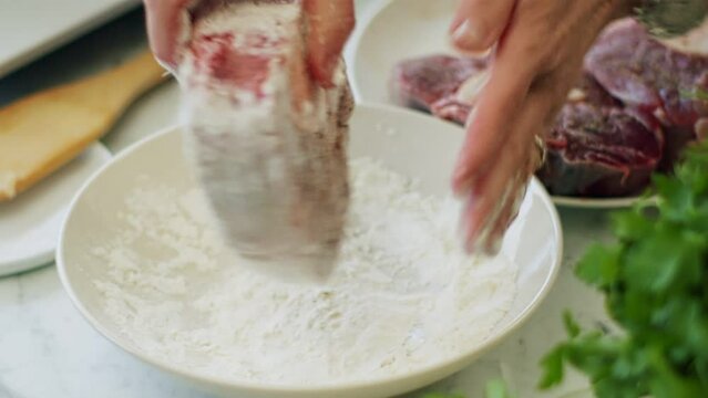 Woman rolling veal shank in flour before frying