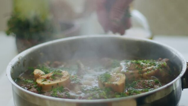 Woman adding greens to stewing ossobuco in frying pan