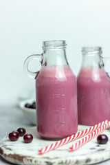 A bottle of cherry smoothies on a white background, cherries in bulk and in a plate. Morning summer breakfast