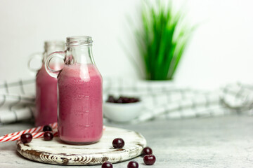 A bottle of cherry smoothies on a white background, cherries in bulk and in a plate. Morning summer breakfast